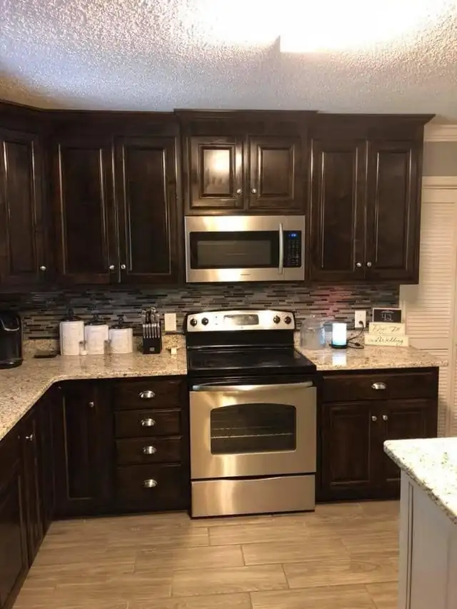 Dark espresso cabinets with speckled granite countertops, glass mosaic backsplash and stainless range