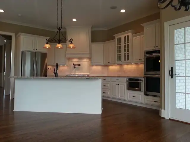Wide view of a white custom kitchen by Swing Cabinets with wall ovens, glass-front uppers and an island