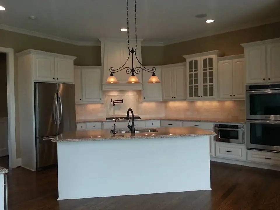 Custom cabinets in Shelbyville, TN by Swing Cabinets: white kitchen with glass-front uppers, double wall ovens, a white island and dark hardwood floors